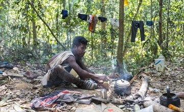 Young man of the Orang Asil tribe sitting on the floor in the jungle and making tea