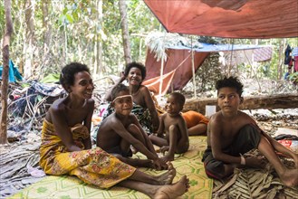 Women and children of the Orang Asil tribe sitting under tarpaulins in the jungle