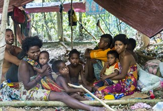 Men women and children of the Orang Asil tribe sitting under tarpaulins in the jungle