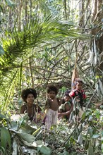 Woman of the Orang Asil tribe sitting with children under palm fronds in the jungle