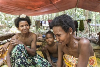 Women and children of the Orang Asil tribe sitting under tarpaulins in the jungle
