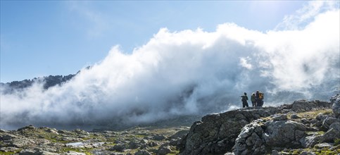 Silhouette of three hikers in front of clouds