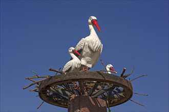 Stork figures on a wagon wheel against blue sky