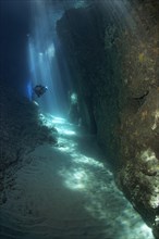Diver in a narrow crevice with sun rays beaming down