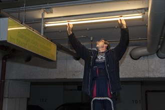 Caretaker replacing fluorescent lamp in underground garage