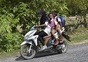 Woman wearing a headscarf with two school children on a scooter