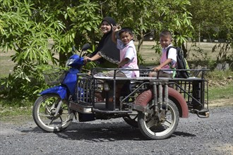 Woman wearing a headscarf and school children on a scooter