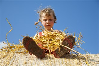 Little girl sitting on a straw bale under a cloudy blue sky
