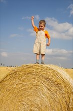 Little boy standing proudly on a straw bale