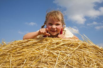 Little girl lying on a straw bale under a cloudy blue sky