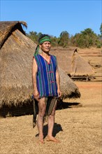 Man in traditional costume in front of a Phnong house