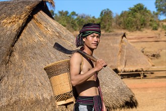 Man in traditional costume in front of a Phnong house