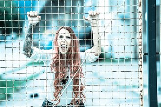 Young woman with long red hair and a tattoo screaming behind bars