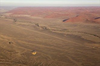 Hot-air balloon above an arid plain and the dry riverbed of the Tsauchab river at the edge of the Namib Desert