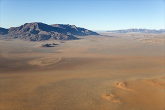 Arid desert plains with so-called Fairy Circles and isolated mountain ridges at the edge of the Namib Desert