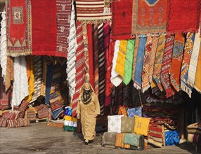 Woman in front of a shop with colourful carpets in the souks of Marrakesh