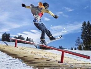 Teenage snowboarder grinding a pole in a funpark