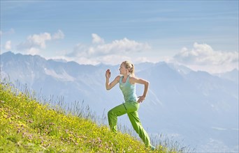 Young woman in her twenties running up field in mountains