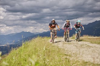 Three mountain bikers with helmets riding on a gravel road