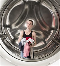 Conceptual image of a young confused man holding laundry inside a washing machine