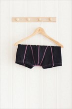 Male black boxer shorts hanging on a clothes hanger in front of white wall