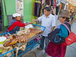 A Quechua Indian woman selling roasted suckling pig and sandwiches on the road