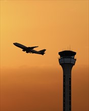 Air traffic control tower with a plane taking off at sunset