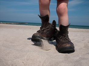 Child wearing large hiking boots on a sandy beach