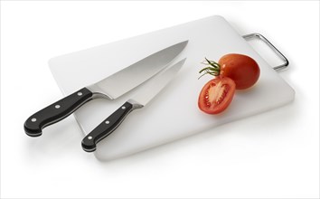 Two knives on a white cutting board with tomatoes