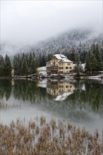 Snow-covered forest and houses reflected in Lake Toblach
