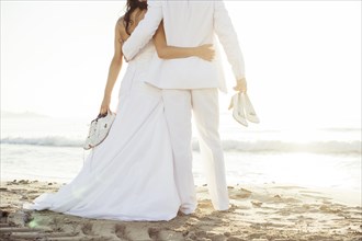 Bridal couple standing arm in arm on the beach