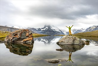 Hiker stands on rocks in the lake and stretches his arms into the air