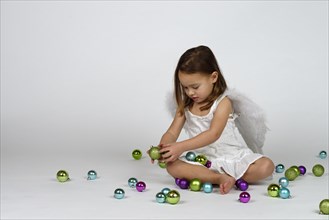 Girl dressed as an angel sits between Christmas baubles