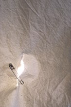 Hole in a sheet being held together by a safety pin