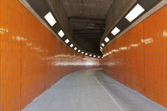 A sidewalk through a brightly lit orange tunnel