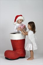 Boy in a Christmas boot handing a small Christmas present to a girl dressed as an angel