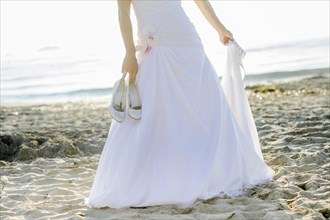 Bride carrying her shoes in her hand on a sandy beach