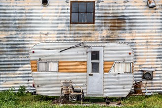 Dilapidated caravan made of corrugated iron parked in front of a corrugated iron wall