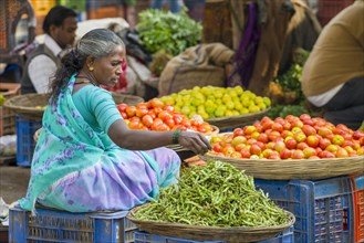 A woman is selling chilis and tomatoes at the weekly vegetable market