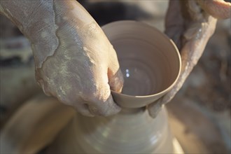 Hands molding a piece of pottery on a wheel head