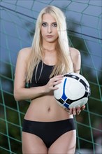 Woman wearing black lingerie posing with a football in a goal