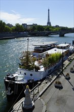 View from Pont Alexandre III bridge across the Seine with houseboats and the Tour Eiffel