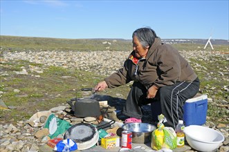 Woman of the Inuit people cooking on a campfire in the tundra