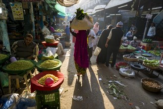 A woman is carrying a bag with vegetables on her head through the vegetable market