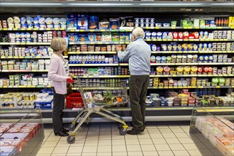 Senior couple shopping with a shopping trolley in the refrigerated dairy section in a supermarket