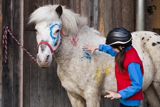 Girl wearing a riding helmet painting a pony with finger paints