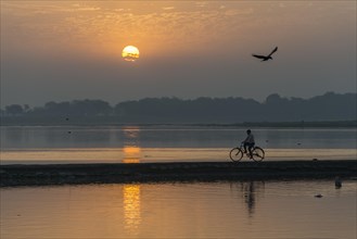 A cyclist crossing the Yamuna river on a dam at sunrise