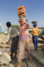 Female construction workers carry bricks on their heads