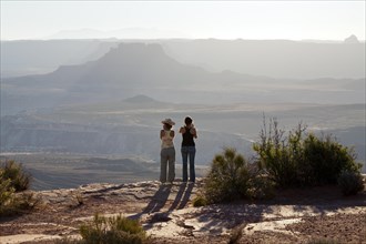 Two tourists on edge of canyon in afternoon light