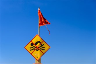 Bathing prohibition sign with red flag in front of a blue sky